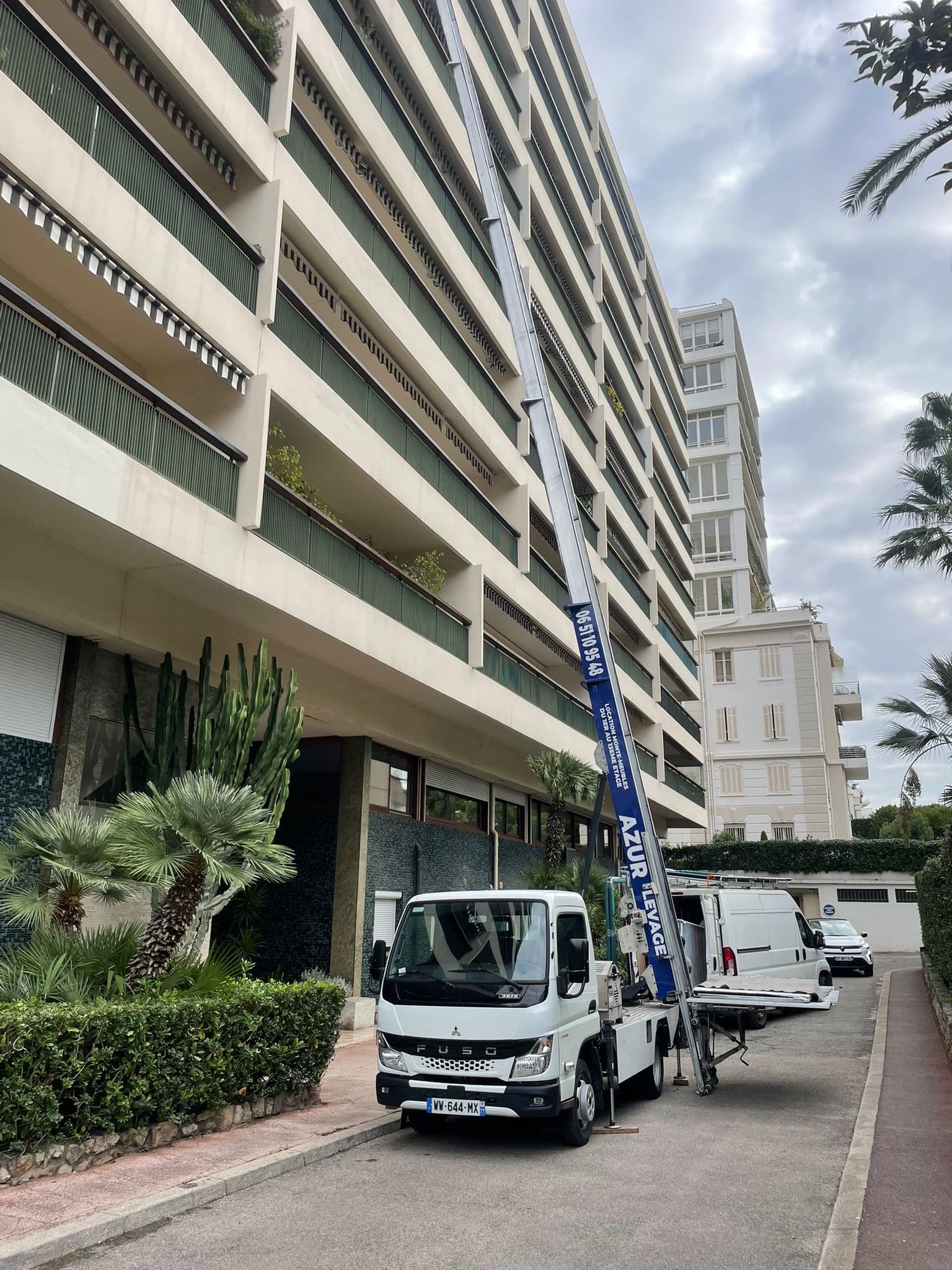 Monte-meuble Azur Levage en action devant un immeuble nicois borde de palmiers